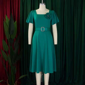 Detail of square neck and floral brooch on dark green flared dress with ruffle sleeves