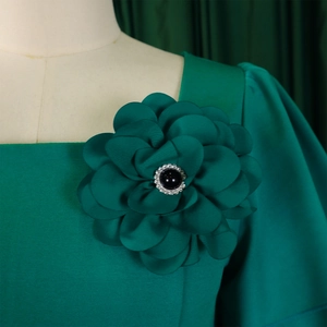 Detailed close-up of dark green satin flower brooch with a central black gem on dress