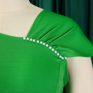 Detail van een smaragdgroene gebreide jurk met gerimpelde schouder en elegante witte parels