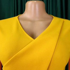 Détail du col en V sur une robe plissée jaune avec tissu en maille texturée sur un mannequin