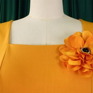 Detail of a large orange fabric flower with a black gemstone on a yellow square-neck dress
