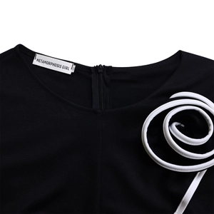Detail of black dress neckline featuring 3D white cord spiral flower and hidden back zipper