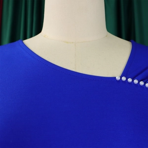 Detail van blauwe jurk met asymmetrische halslijn en decoratieve parels op de schouder