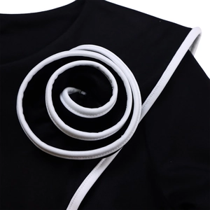 Detail of black dress with white spiral decorative trim and high-contrast stitching
