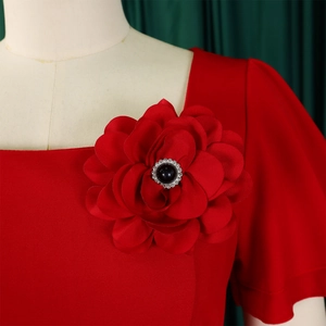 Detail of the oversized red fabric flower with a black bead and crystal center on the neckline