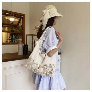Detail of white canvas shoulder bag featuring floral lace crochet and a delicate ribbon bow