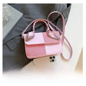 Top view of pink paneled crossbody bag with ribbon handle next to iPhone for size scale