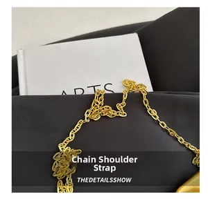 Close-up of a polished golden chain shoulder strap on a textured black woven handbag