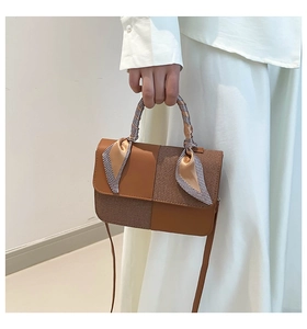 Detail of a brown checkered leather handbag with a silk scarf wrapped around the handle