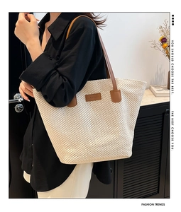 Détail du sac cabas en paille tressée avec anses en cuir marron et écusson de mode