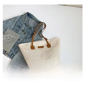Détail du sac cabas tissé avec anses en cuir marron et étiquette mode sur fond neutre