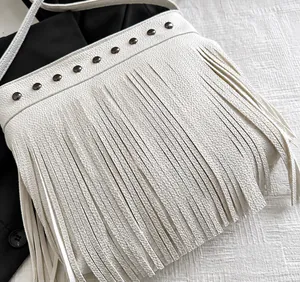 Detalle de bolso tipo cubo blanco en piel granulada con flecos y remaches metálicos