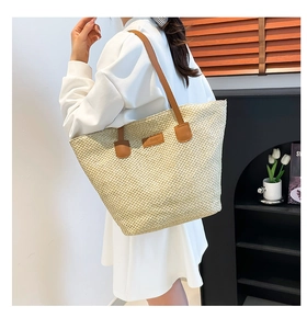 Gros plan du sac cabas en paille tressée avec empiècement en cuir et bandoulière longue