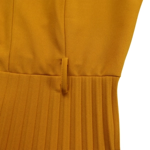 Détail macro du tissu plissé jaune moutarde et des passants de ceinture de la robe