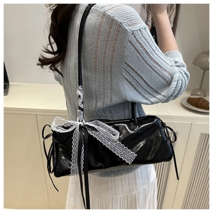Detalle de bolso de hombro en charol negro con encaje blanco y lazo de seda