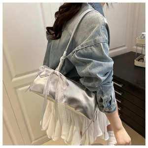 Detalle del bolso cilíndrico plateado con un lazo decorativo de encaje blanco en el asa