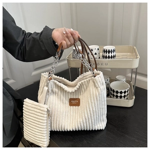 Close-up of white corduroy tote bag with brown leather label and silver chain handle