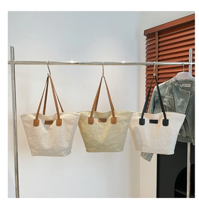 Trois grands cabas en paille tissée de couleurs variées suspendus sur un portant