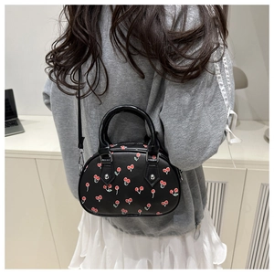 Detail of black PU leather handbag featuring red cherry prints and silver metallic studs