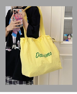 Detail of yellow nylon tote bag featuring green Daximo letter print and drawstring top