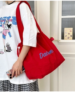 Close-up of red canvas tote bag with blue Daimm lettering and white drawstring detail