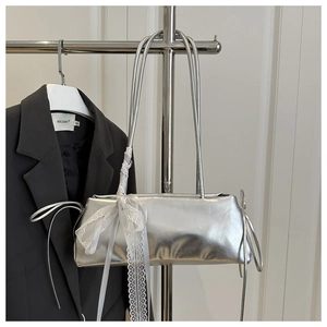 Detalle de bolso plateado metalizado con lazo de encaje blanco y correas dobles
