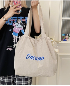 Detailed view of beige drawstring tote bag with blue Daiximo embroidered lettering