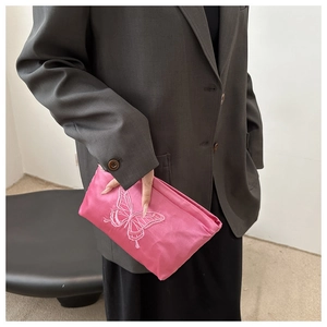 Dettaglio della borsa da trucco in raso rosa con ricamo a farfalla tenuta da una modella