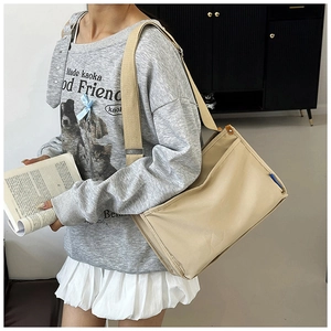 Detail of a beige canvas messenger bag with wide shoulder strap used in a casual campus setting