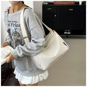 Detail view of white canvas crossbody bag with wide shoulder strap and blue side label tag