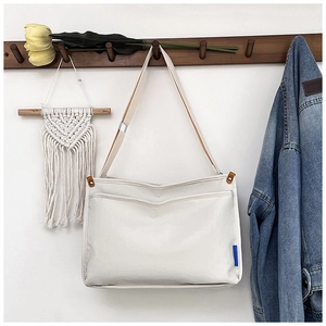 Detail view of cream canvas messenger bag hanging on wall with blue logo tag