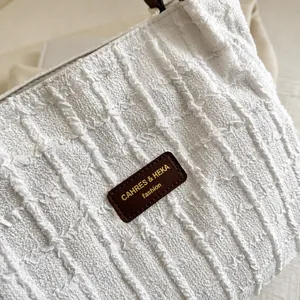 Detail van witte getextureerde stoffen draagtas met een luxe lederen logo patch