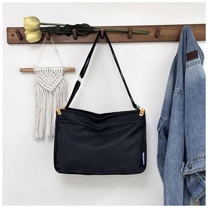 Detail of minimalist black nylon messenger bag hanging on a wooden coat rack
