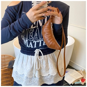 Close-up of brown leather pleated croissant bag worn as a mini crossbody accessory