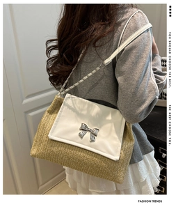 Detail of woven straw shoulder bag featuring a white leather flap and silver metal bow