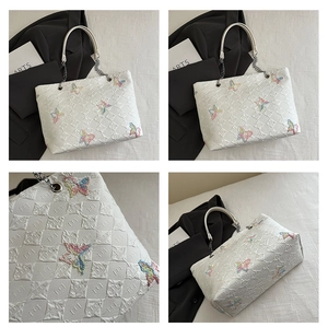 Detail view of white quilted tote bag featuring colorful butterfly embroidery and chain straps