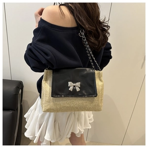 Detail of woven straw shoulder bag with black leather flap and silver bow clasp