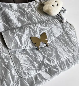 Detail of silver pleated shoulder bag featuring a metallic butterfly buckle and cloud charm
