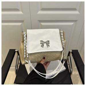 Close-up of woven straw shoulder bag featuring white leather flap and silver bow detail