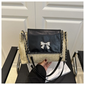 Detail of woven straw shoulder bag with black leather flap and silver bow clasp buckle
