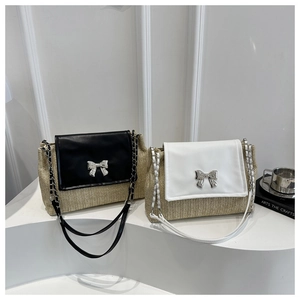Detail of straw crossbody bag showing the metallic bow buckle and leather chain strap
