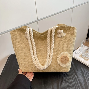 Borsa tote in paglia intrecciata con girasole, manici in corda e nappe sul tavolo