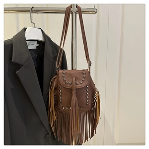 Detail view of brown fringe crossbody bag with metal rivets on a vintage leather surface