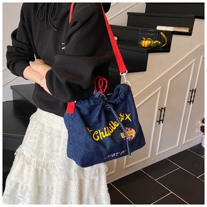 Detail of blue denim tote bag with yellow embroidery and red woven shoulder strap