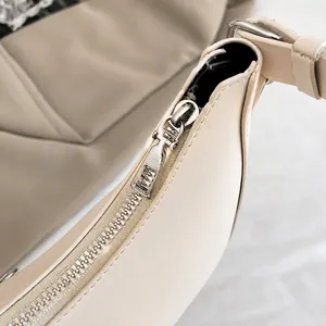 Close-up of the smooth silver metal zipper and stitching on the off-white crescent bag