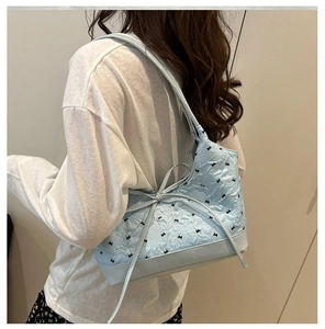 Detalle del bolso tipo cubo azul claro con tela jacquard floral y bordado de lazo negro