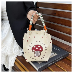 Close-up of knit bucket bag featuring mushroom embroidery and colorful woven handles