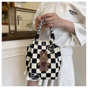 Detail of knitted checkerboard bucket bag with cute rabbit pattern and woven handle