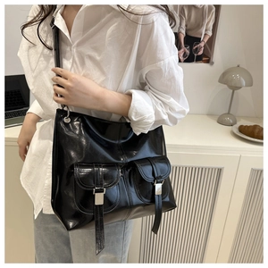 Detail view of large black glossy tote bag with dual front pockets and silver buckles