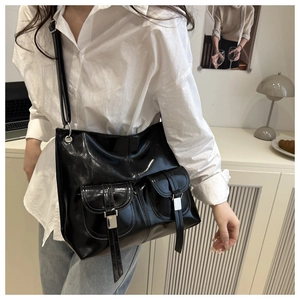 Detail of black faux leather motorcycle tote bag with silver buckles worn by a model